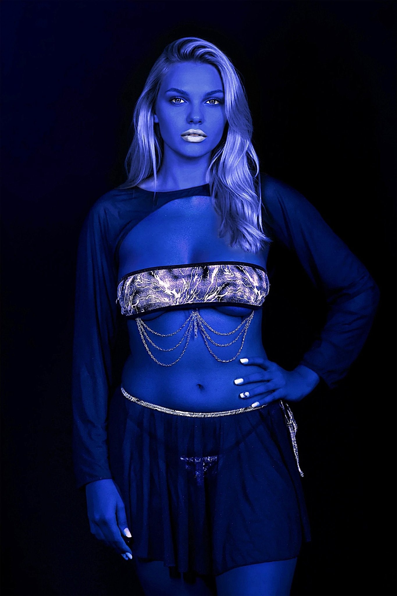 A woman with blue-toned skin and blonde hair poses in the Electric Glint Fairy Skirt by Brigitewear International, LLC, styled with a metallic crop top and gold chains.