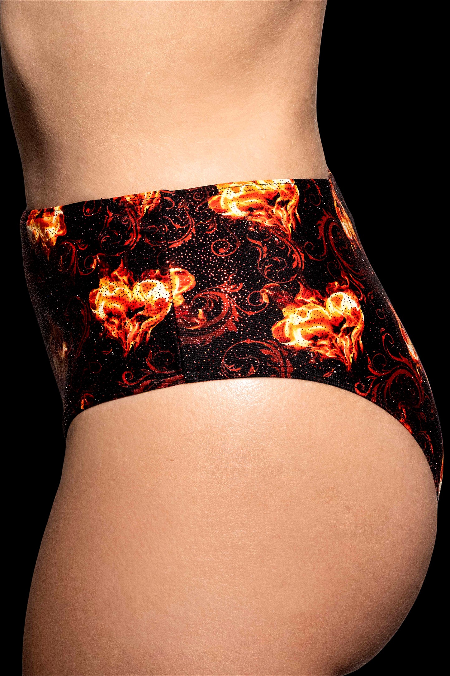 Side view of a person wearing Brigitewear International, LLC's Inferno Heart High Waist Bottoms—black underwear with a fiery flame pattern—against a black background.