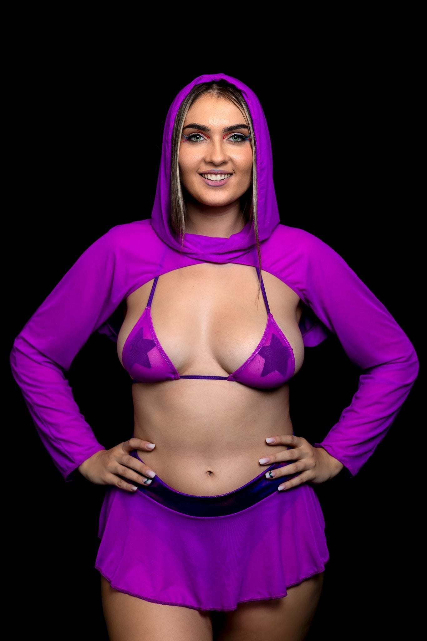 A smiling woman models the Brigitewear International, LLC Grape Babe Mesh Micro Triangle Top with a matching skirt and hood, standing against a black background.
