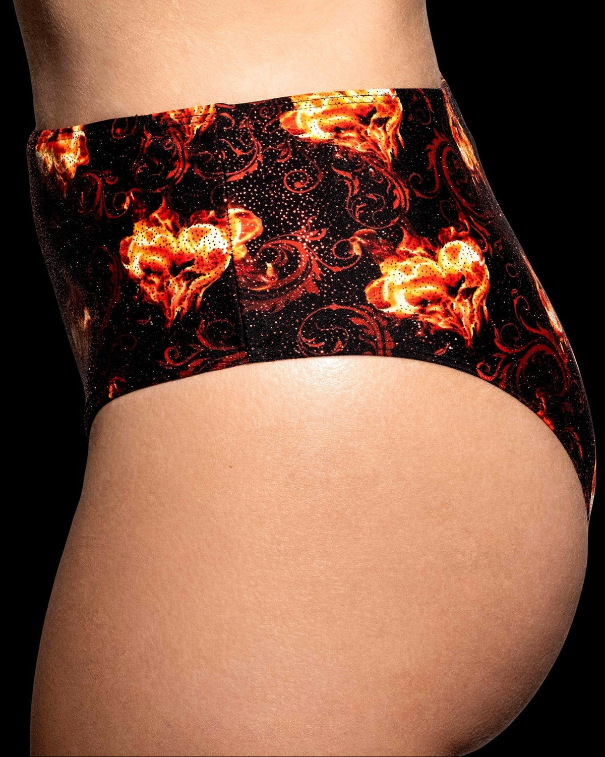 Model wears Brigitewear International’s Inferno Heart High Waist Bottoms in black, featuring a red and orange flaming heart pattern—side view.