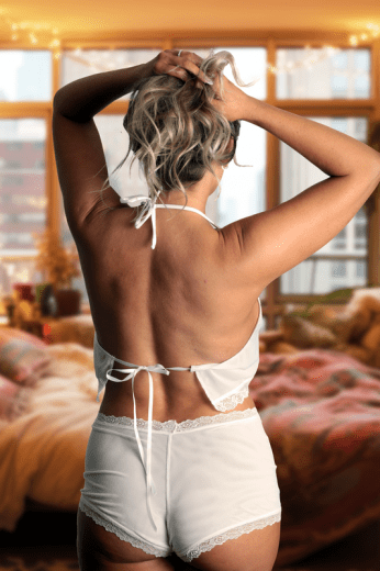 Model wears Malibu Nights Boy Shorts by Brigitewear International, LLC in a cozy bedroom, standing with her back to the camera as she fixes her hair.