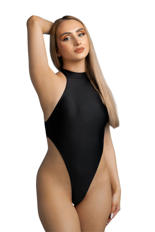 A woman with long blonde hair models the Vesper High Cut One Piece by Brigitewear International, LLC, posing with one arm raised against a white background.