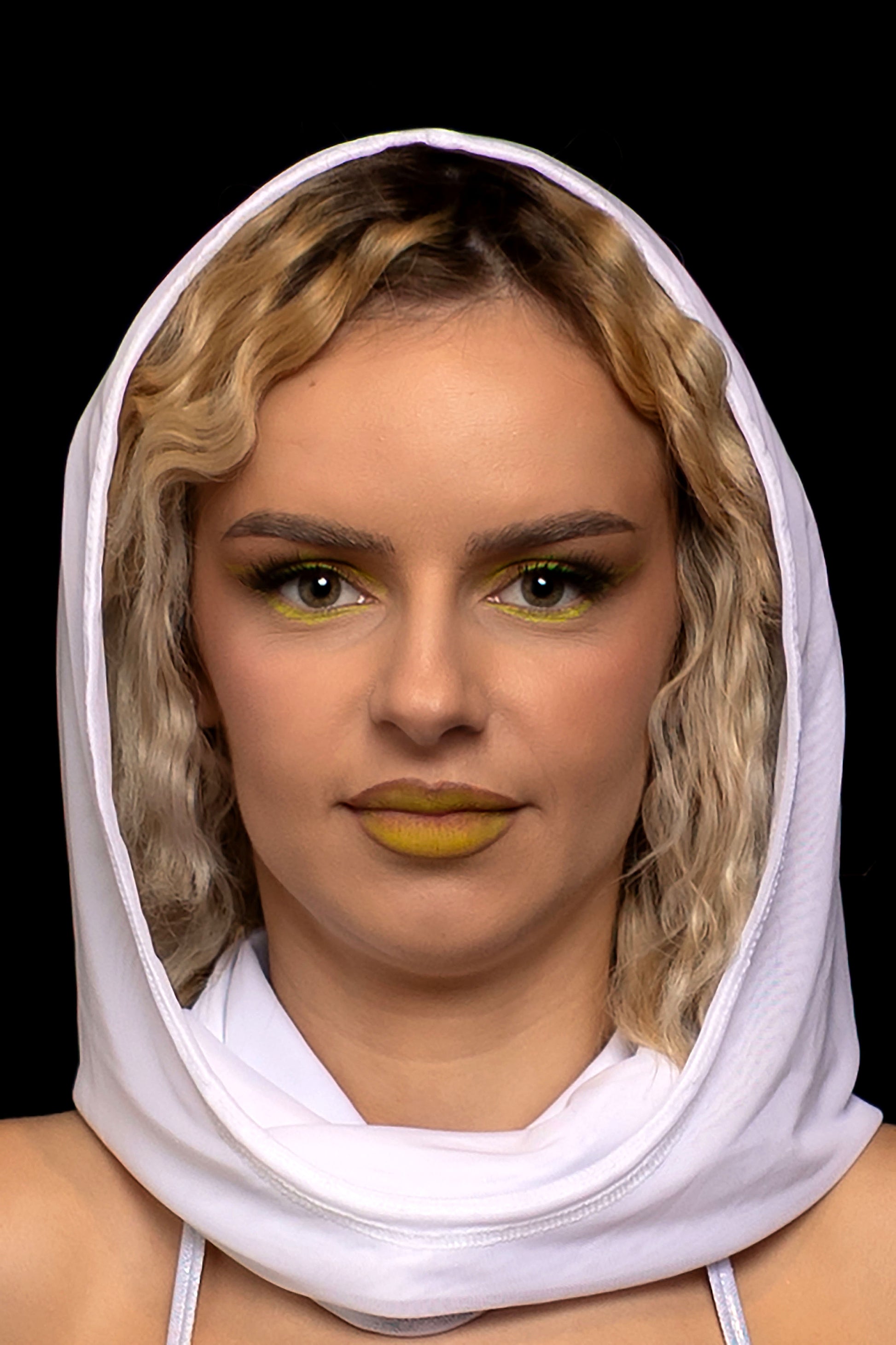 A woman with wavy blonde hair, yellow makeup, and a Brigitewear International, LLC White Mesh Hood poses against a black background.