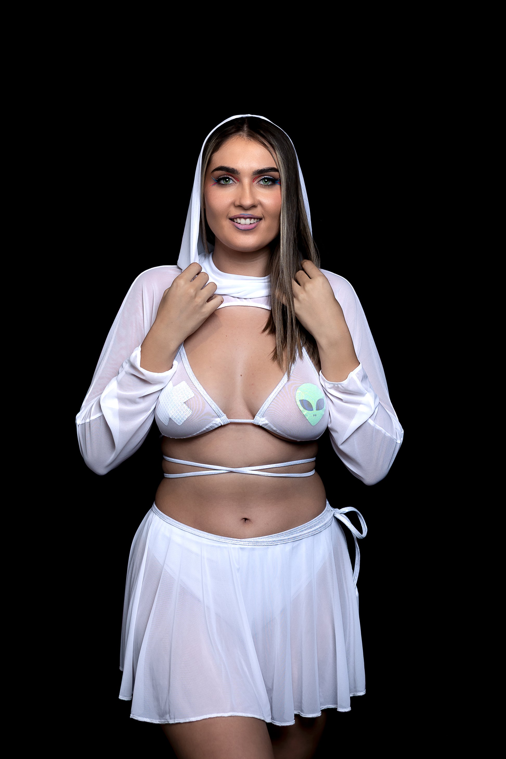 A woman smiles in a sheer white Brigitewear International Dreamy Circle Skirt and crop top adorned with cross and alien symbols.