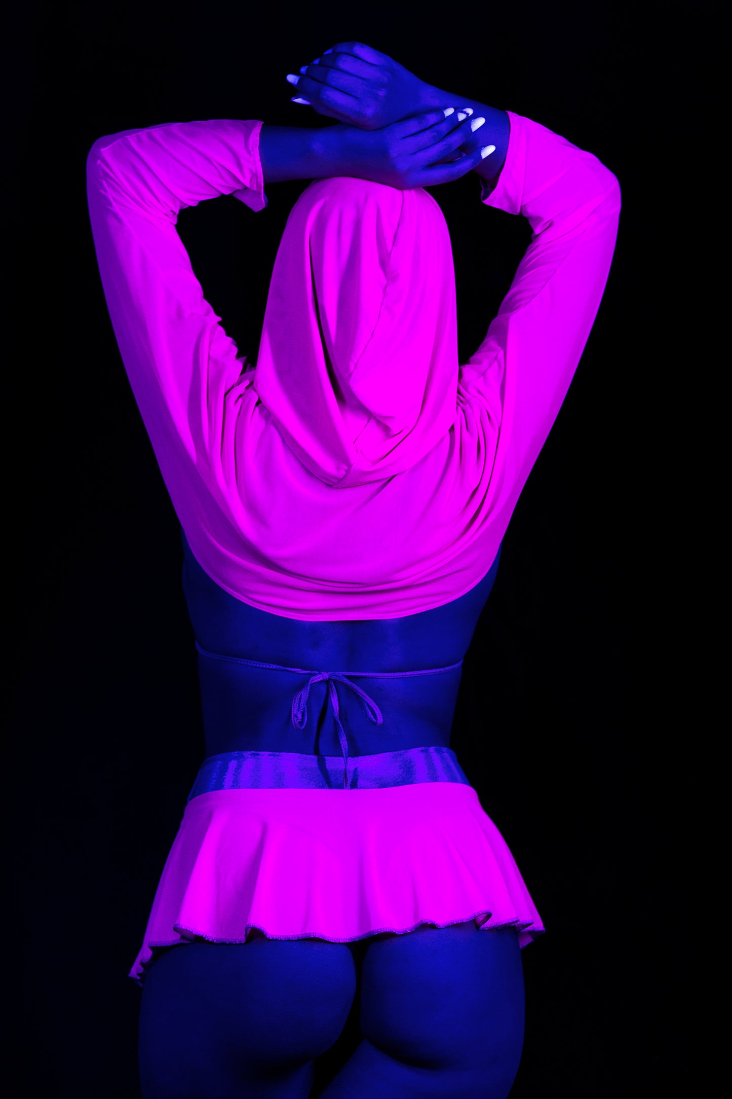 Model wears the Grape Babe Hooded Mesh Shrug by Brigitewear International, LLC, striking a pose with arms raised under vibrant blue and pink lighting.