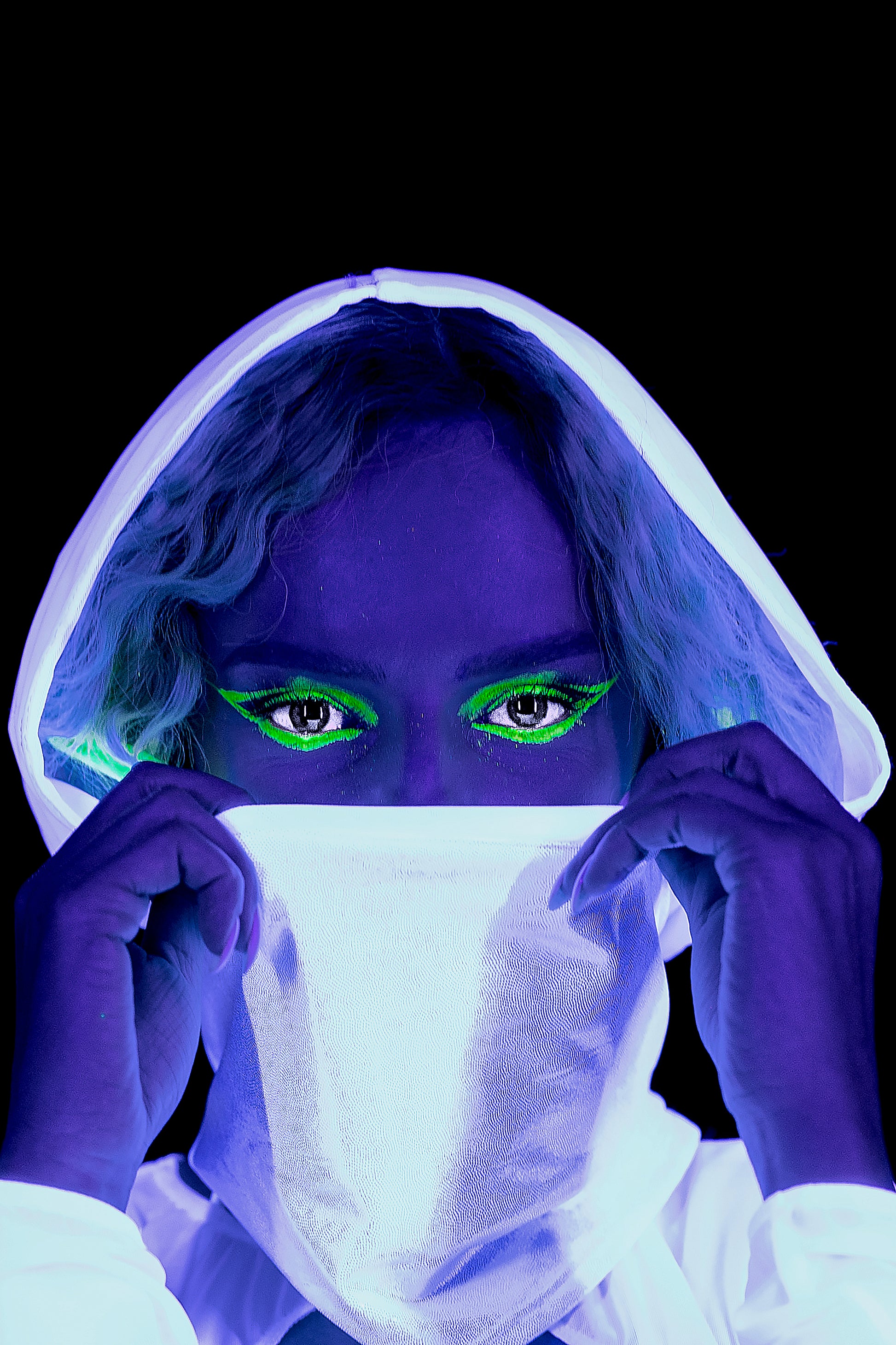 A person wears the White Mesh Hood by Brigitewear International, LLC, featuring neon green eye makeup and glowing under blacklight.