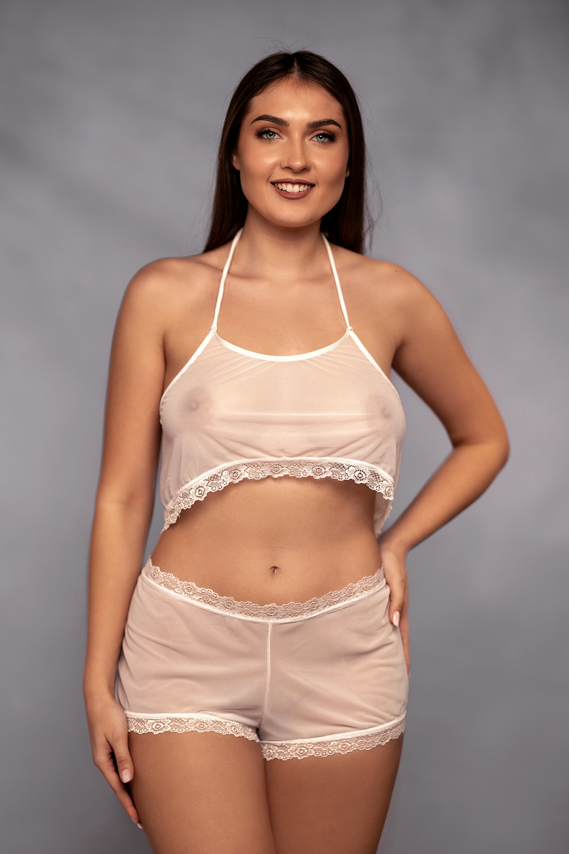 A woman smiles against a plain background, wearing Brigitewear International's Malibu Nights Boy Shorts and a sheer white lace camisole.