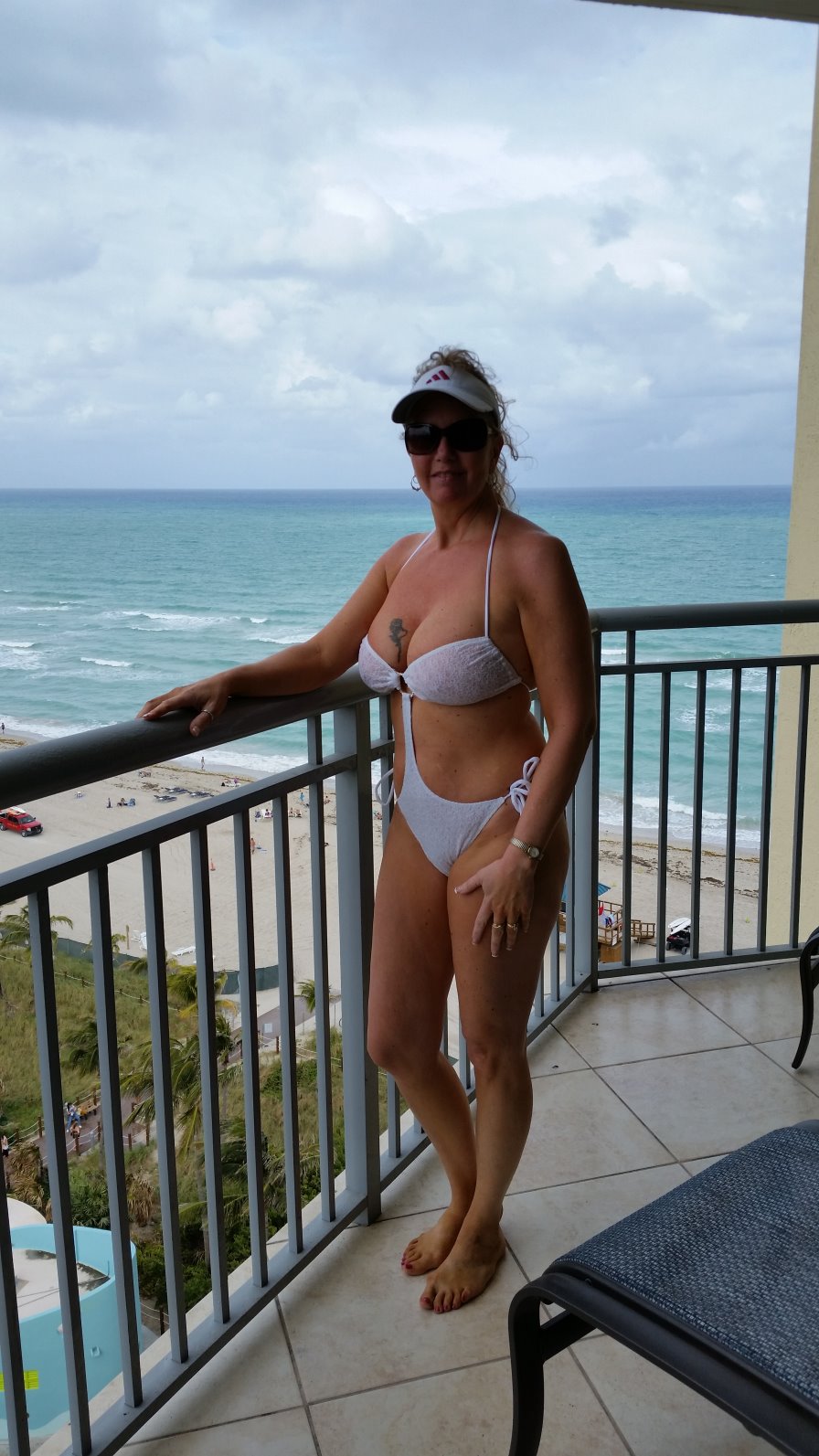 Woman wearing a white cut-out bikini standing on a balcony overlooking the ocean