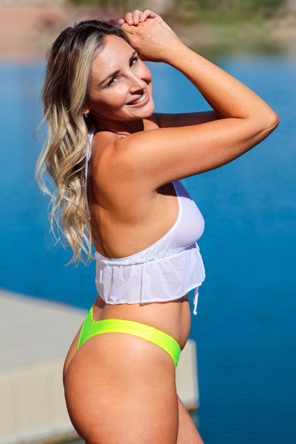 A smiling woman wears the Brigitewear International, LLC Front Tie Halter in white and neon green bikini bottoms while posing by the water on a sunny day.