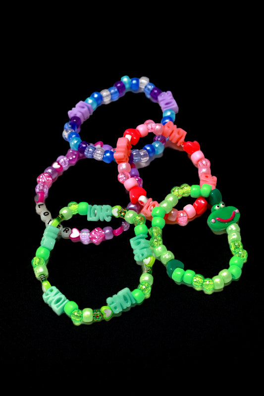 Baby's 1st Kandi by Brigitewear International, LLC: Four colorful beaded bracelets featuring letter beads that spell words like LOVE, displayed on a black background.