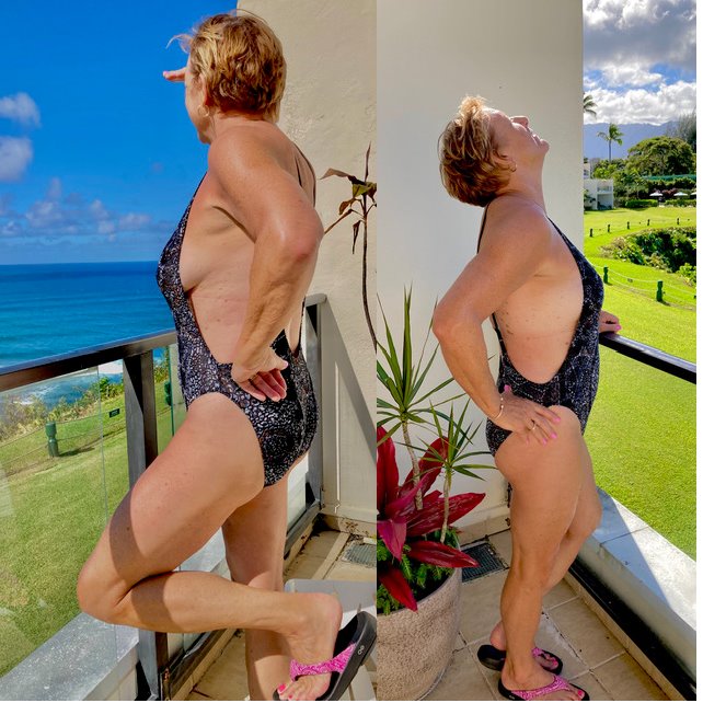 A woman in a swimsuit poses on a balcony overlooking the ocean and a grassy landscape on a sunny day.