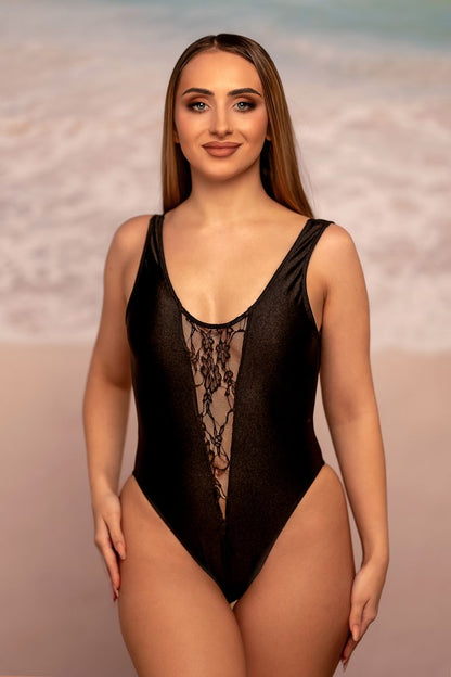 Woman wearing the Bliss One Piece by Brigitewear International, LLC, stands on a sandy beach with the ocean in the background.