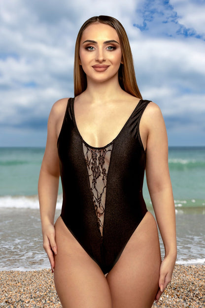 Woman in the Bliss One Piece by Brigitewear International, LLC stands on a beach, ocean and cloudy sky behind her.