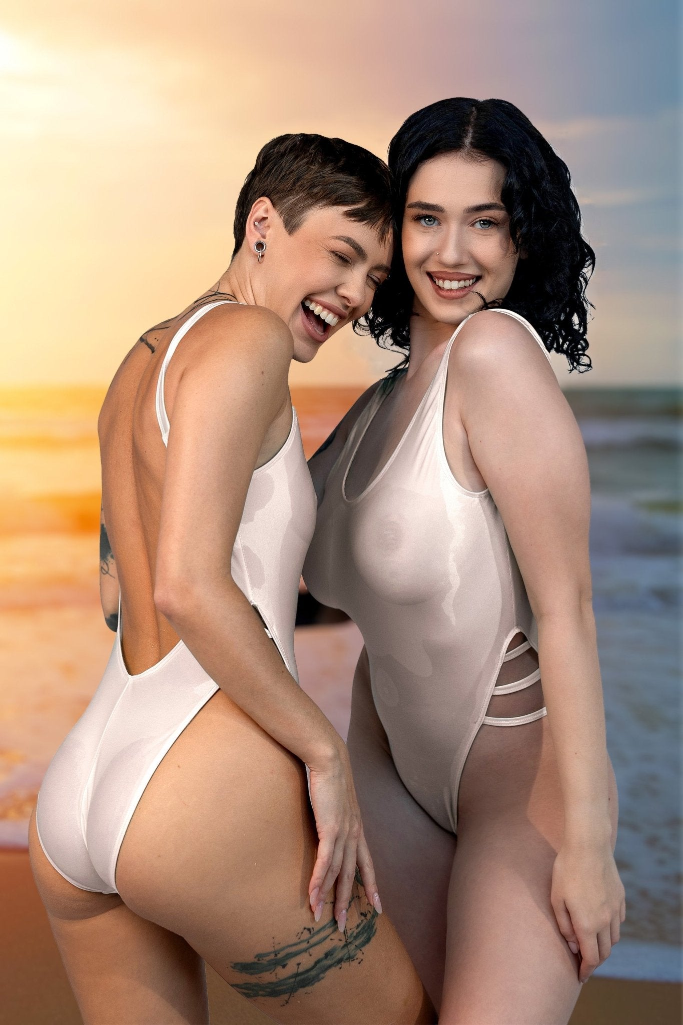 Two women in Breezy See Through One Piece Swimsuits by Brigitewear International, LLC smile and pose together on a beach at sunset.