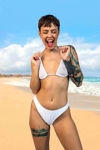 A woman smiles and poses playfully on a sunny beach with waves in the background, wearing the Cannes Mesh See Through Bikini Top by Brigitewear International, LLC.