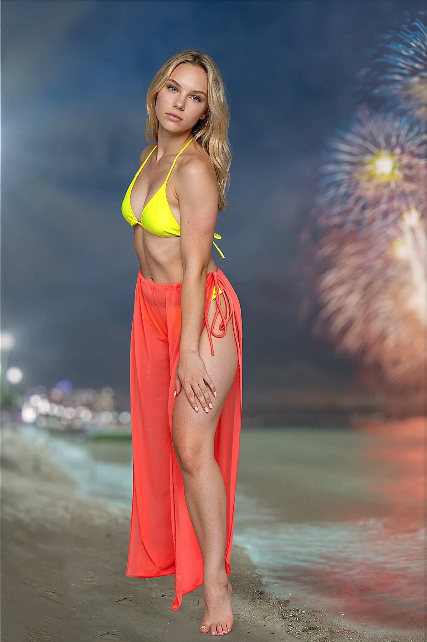 A woman wearing Brigitewear International’s Coachella Pants – Sheer Tie Side Festival Mesh Cover-Up stands on a beach at night with fireworks in the background.