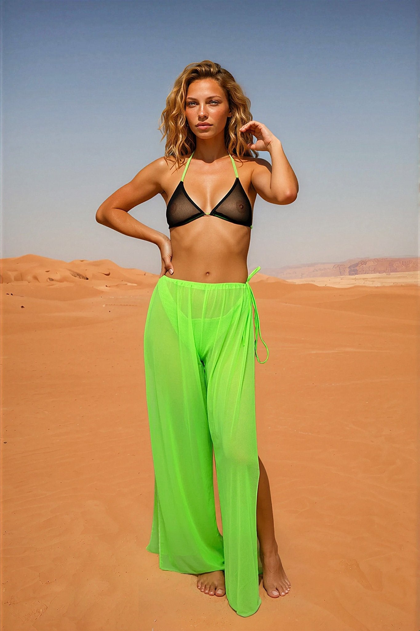 Woman wearing Brigitewear International, LLC Coachella Pants – Sheer Tie Side Festival Mesh Cover-Up in neon green, paired with a black mesh bikini top, stands in a sandy desert and looks at the camera.