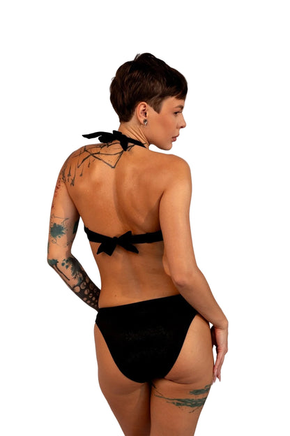 A woman with short hair and tattoos models Brigitewear International, LLC's Ecstasy Bottoms—sexy and stylish bikini bottoms—posing with her back to the camera.