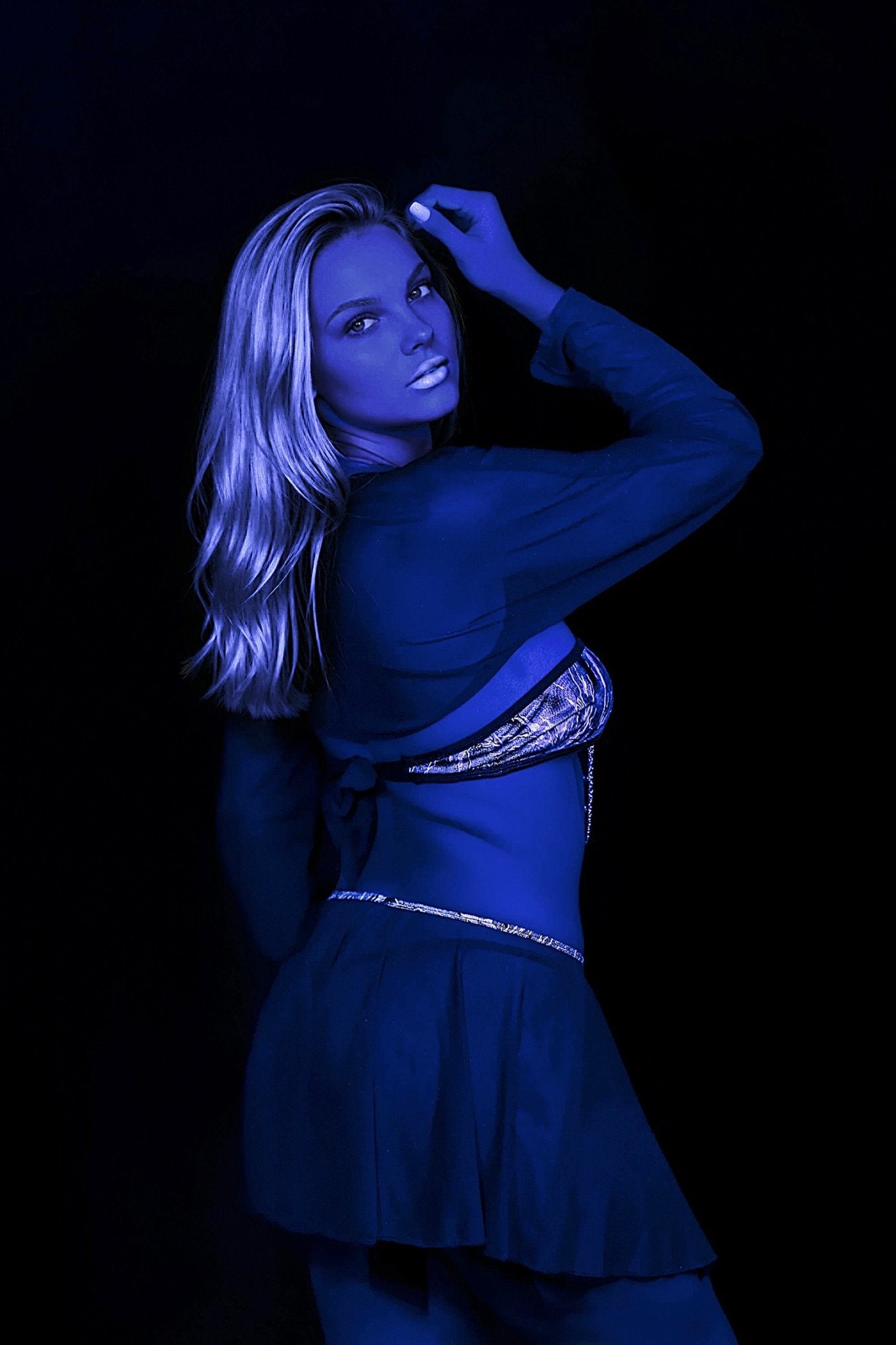 A woman poses in the Electric Glint Fairy Skirt by Brigitewear International, LLC against a black background, with a blue tint on her skin and clothes.