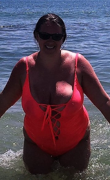 Woman in a bright pink Brigitewear swimsuit standing in shallow ocean water on a sunny day.