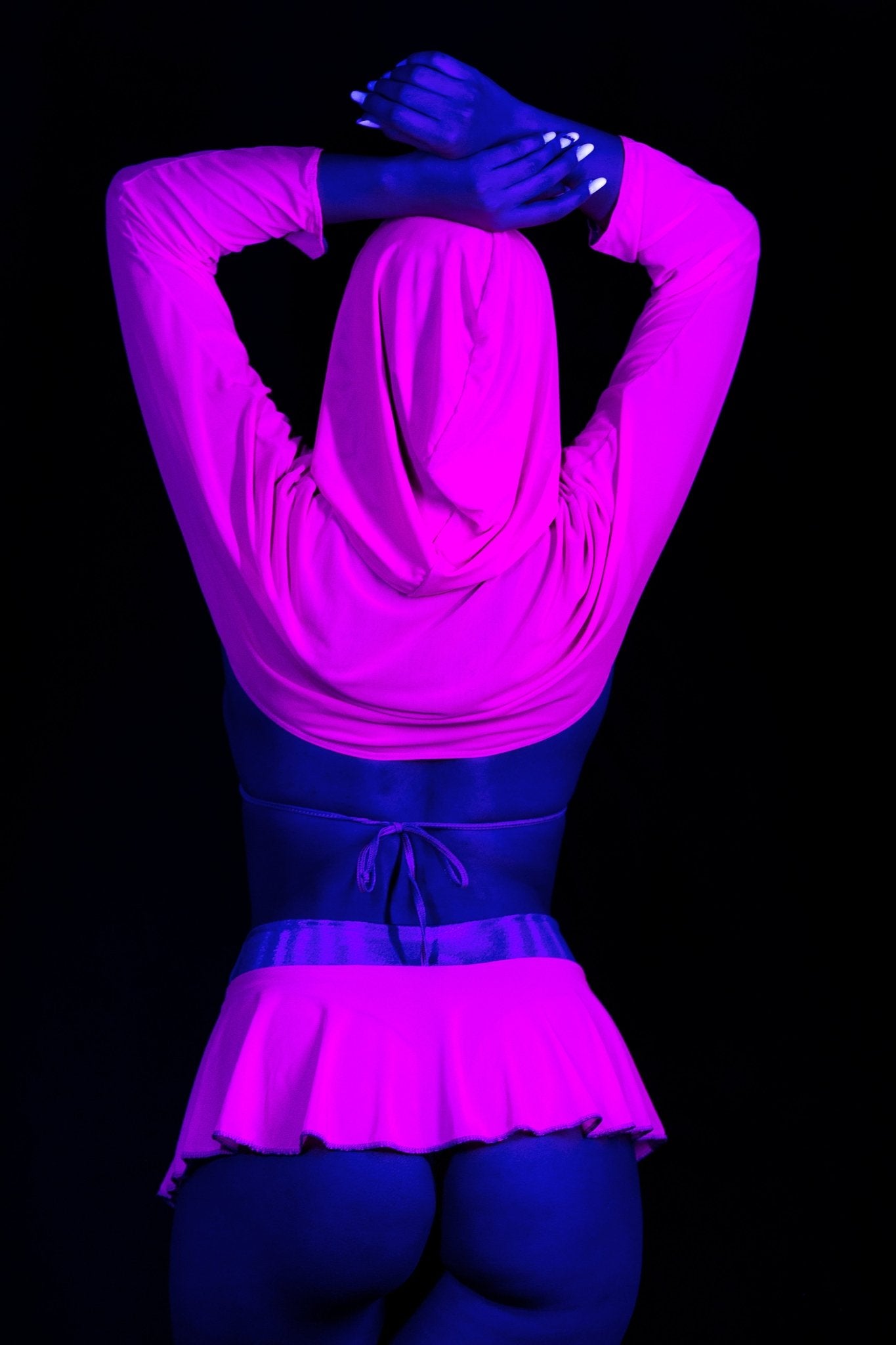 Model wearing Brigitewear International, LLC’s Grape Babe Flirt Skirt-Sexy Swim Skirt Cover Up poses with raised arms under dramatic blue and pink lighting.