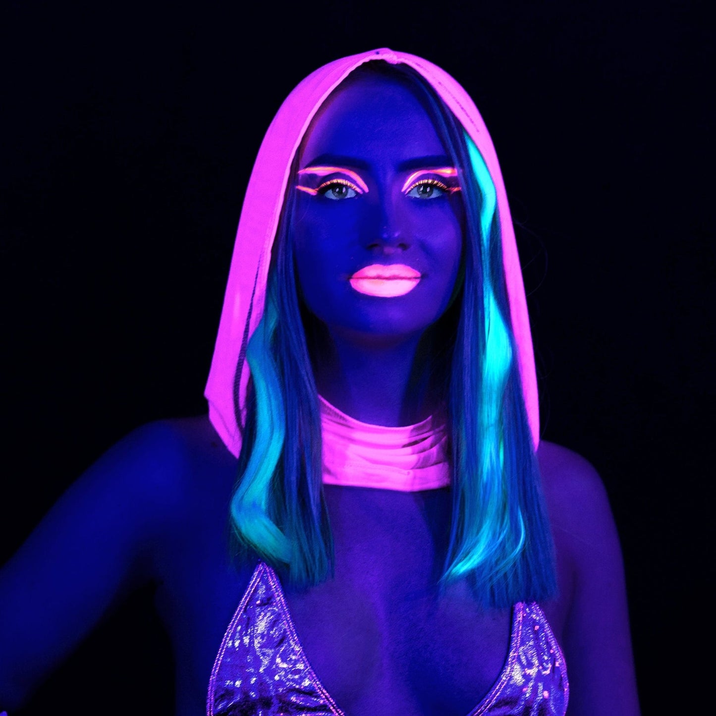 Wearing the Grape Babe Mesh Hood by Brigitewear International, LLC, a person with neon face paint and glowing makeup stands under blacklight against a dark background.