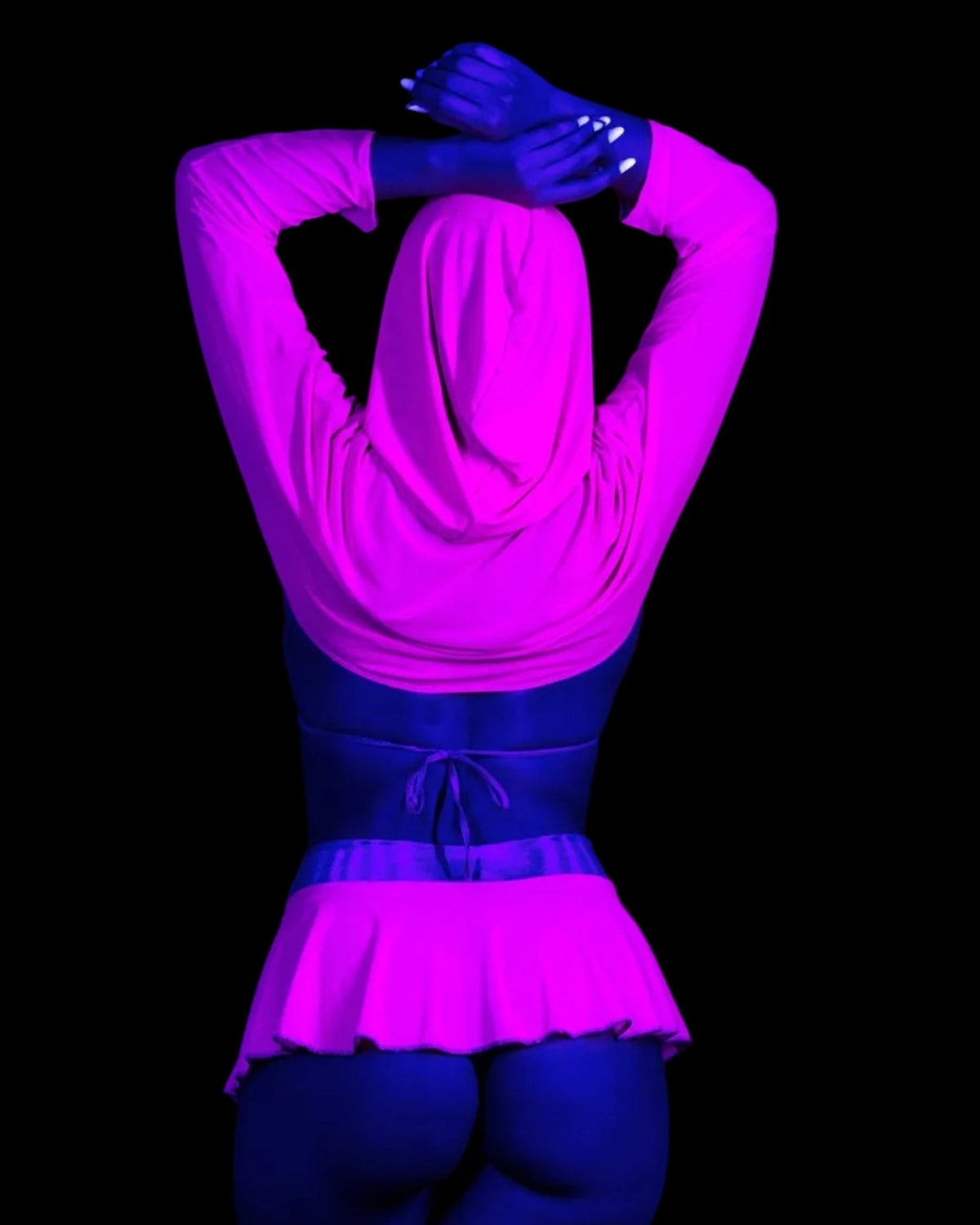 A person wears a Grape Babe Mesh Hooded Shrug, bikini top, and pleated skirt against a black background.