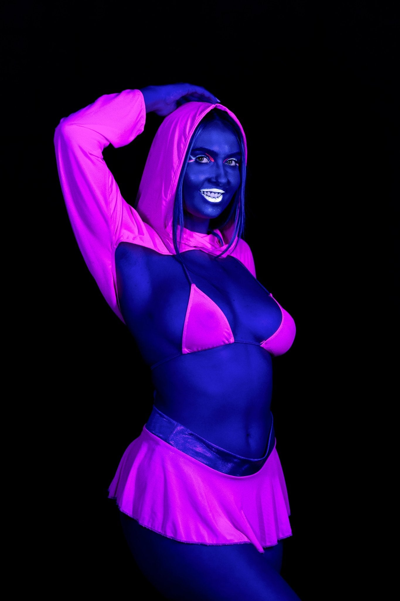 A woman wearing the Brigitewear International, LLC Grape Babe Mesh Micro Triangle Top glows under blacklight against a dark background.