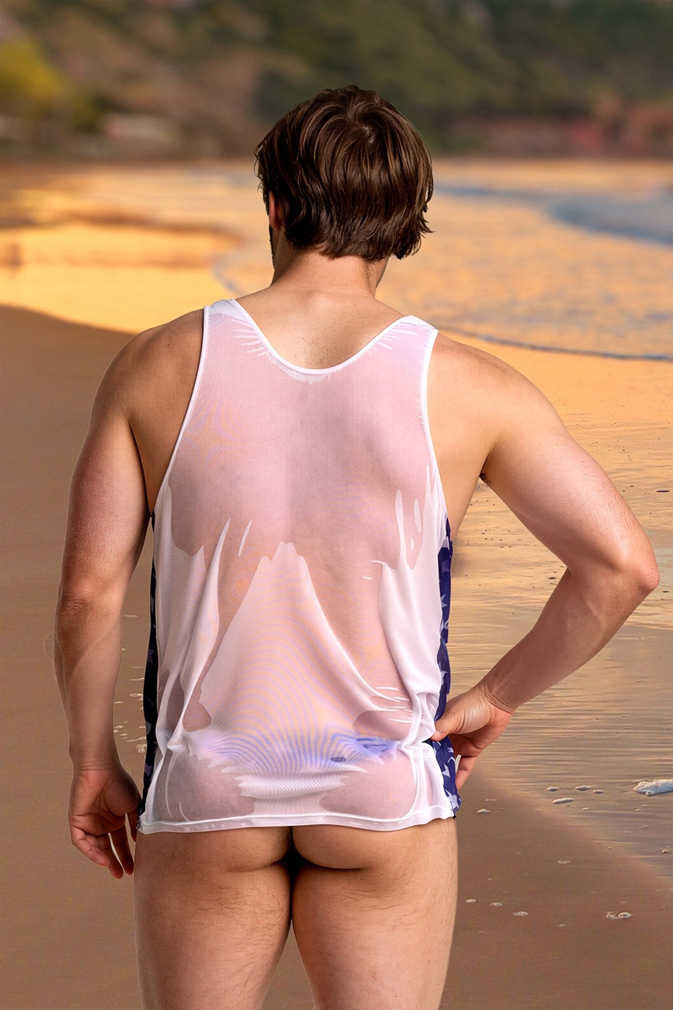 A man wearing the Independence Men's Tank Top by Brigitewear stands on the beach, facing the ocean with his back to the camera.