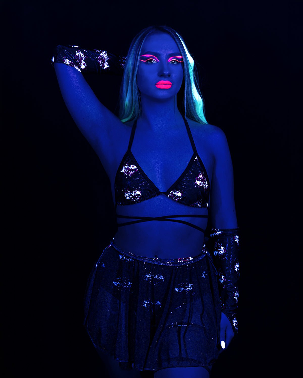 A person in a black Inferno Heart Open Skirt-Rave Festival, bikini top, and arm warmers under neon UV lighting.