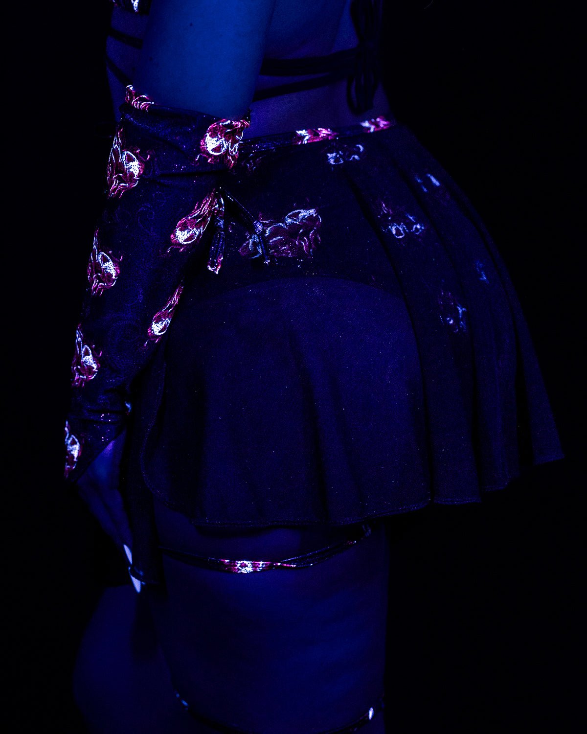 Inferno Heart Open Skirt-Rave Festival: black pleated mini skirt with a pink heart pattern, worn under black light.