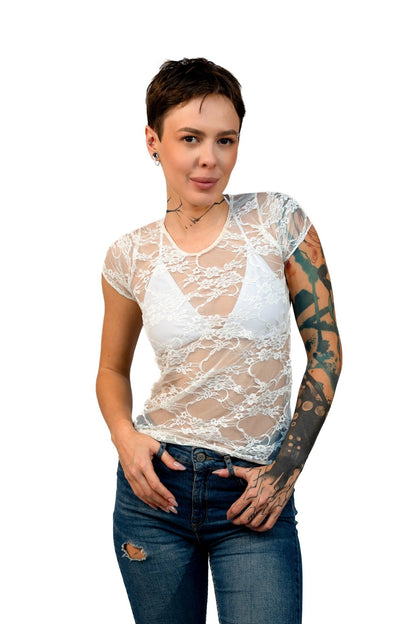 A tattooed model wears the Brigitewear International Long Sheer Lace Tee over a white bralette and blue jeans, posing against a white background.