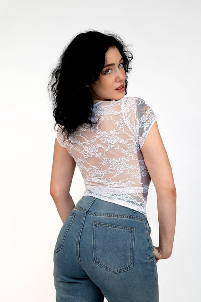 Woman with curly black hair models the Brigitewear International, LLC Long Sheer Lace Tee, paired with blue jeans, against a plain white background.