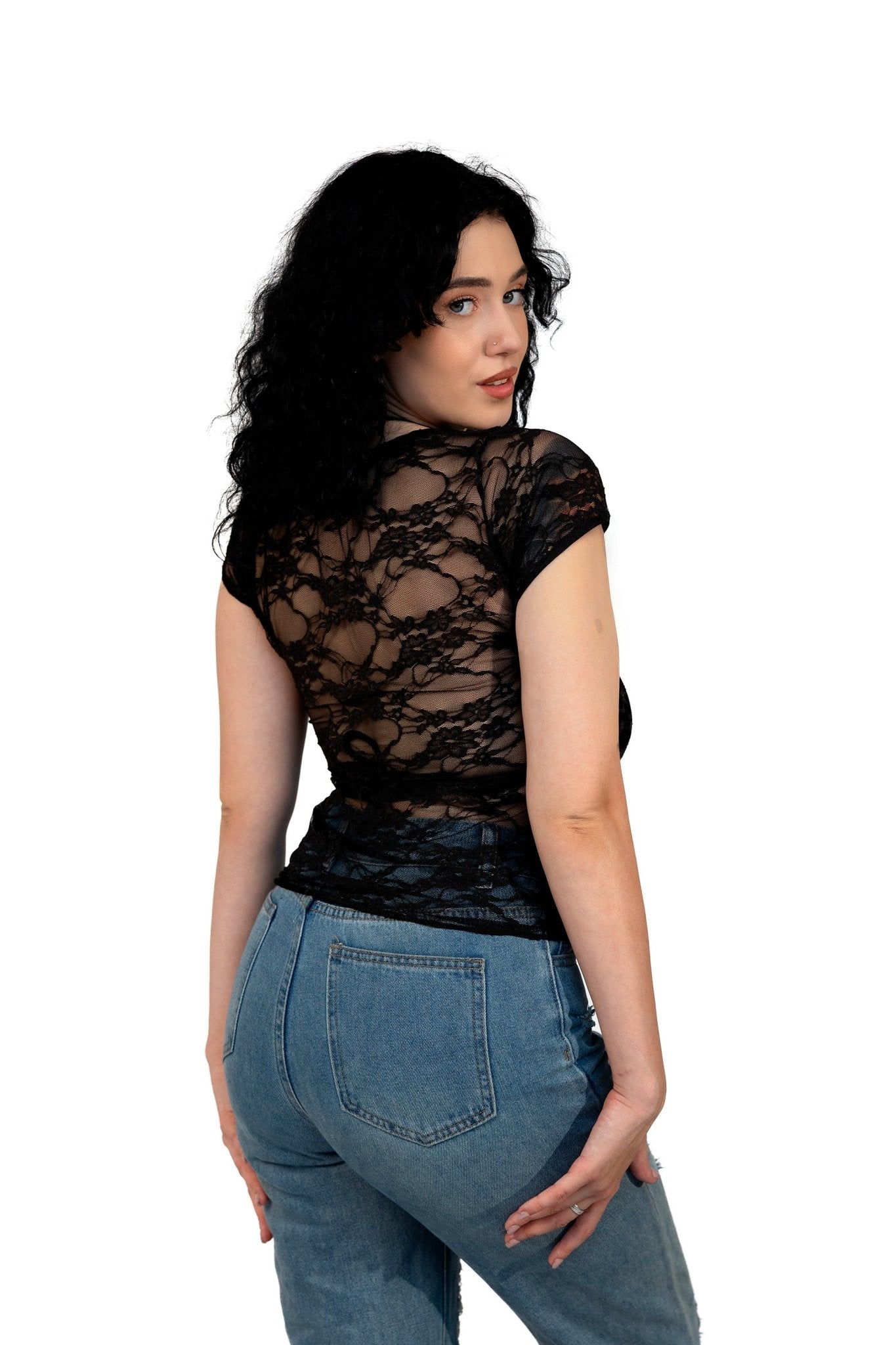 A woman with long curly dark hair poses in the Brigitewear Long Sheer Lace Tee by Brigitewear International, LLC, paired with blue jeans.