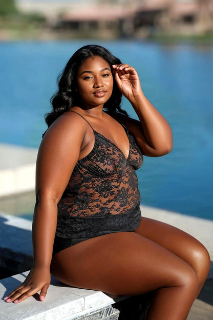 A woman wears the Lovely Lace Halter Sheer Top by Brigitewear International, LLC, sitting by the waterfront and confidently touching her hair while looking at the camera.