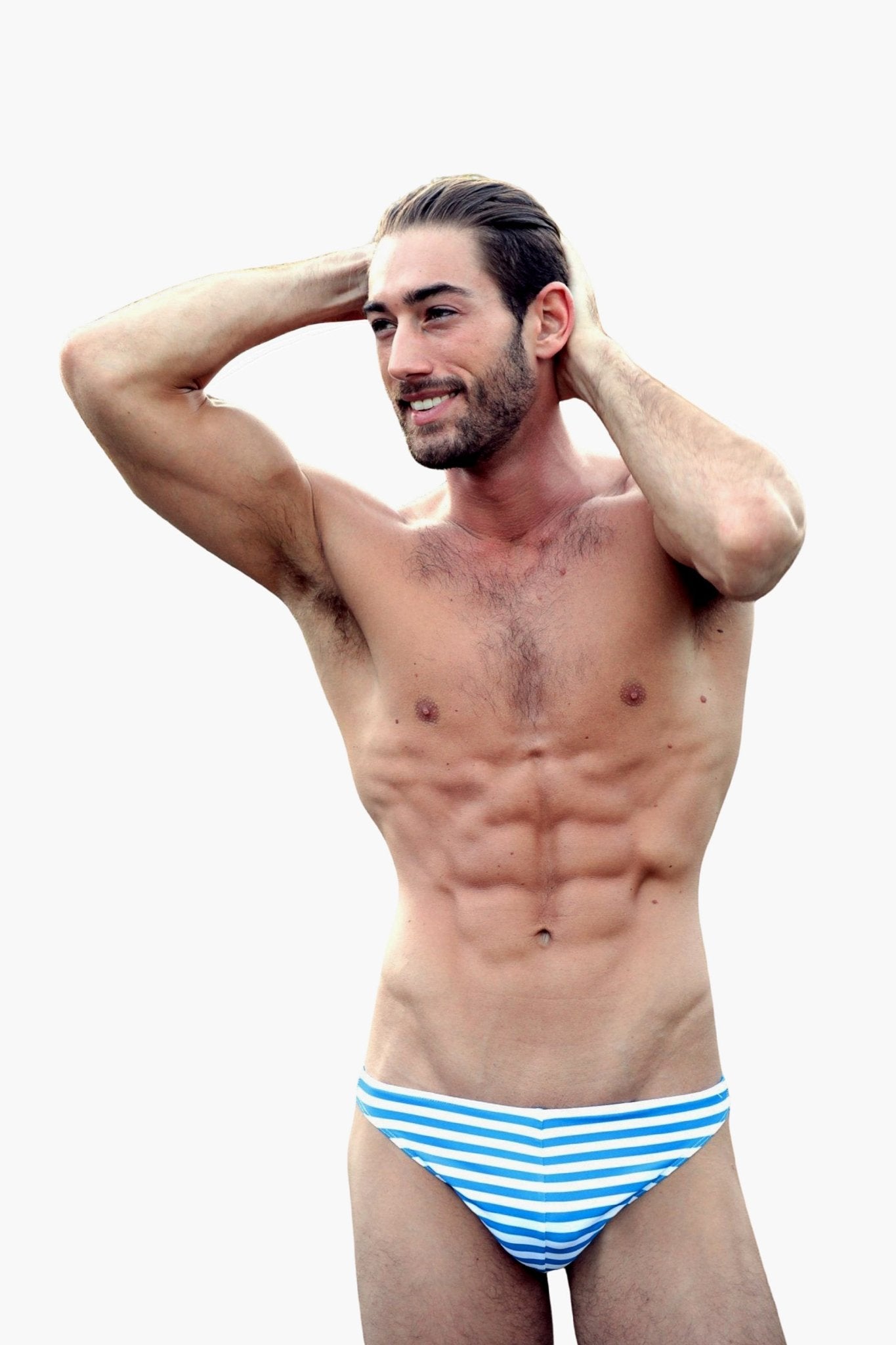 Smiling man models the Brigitewear International, LLC Low Rider Men's Thong in blue and white stripes, posing with hands behind his head against a plain background.