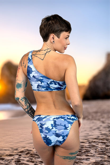Woman wearing the Brigitewear Camo Cannes Ocean Wave Asymmetrical Top by Brigitewear International, LLC stands on a sandy beach at sunset, showing off her tattoos as she faces away.